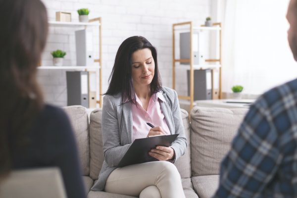 Professional psychologist taking notes at couple meeting with patients
